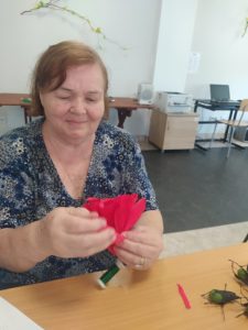 seniorka Dziennego Domu Pomocy formuje maki z płatków z krepiny na zajęciach terapii zajęciowej