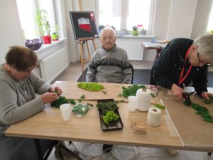 seniorzy Dziennego Domu przygotowują kompozycję z mchu na zajęciach ergoterapii