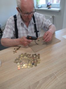 Senior Dziennego Domu Pomocy przygotowuje kompozycję z monet na zajęciach ergoterapii