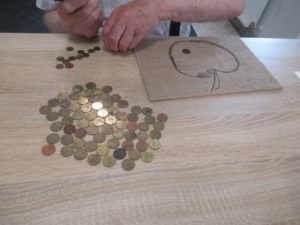 Uczestnik Dziennego Domu Pomocy przygotowuje kompozycję z monet na zajęciach ergoterapii