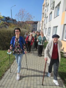 opiekun wspólnie z seniorami Dziennego Domu Pomocy dla Osób Starszych w Jaśle spacerują z kijkami do nordic walking