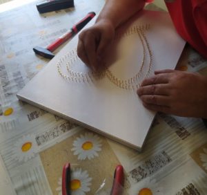 senior Dziennego Domu Pomocy w Jaśle przygotowuje obraz do wykonania techniką string-art z logo MOPS w Jaśle