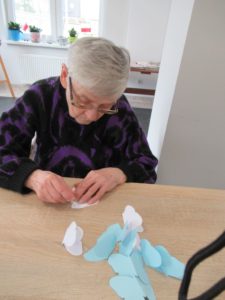 seniorka Dziennego Domu Pomocy skleja papierowe elementy girlandy na zajęciach arteterapii