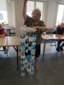 seniorka Dziennego Domu prezentuje girlandę wykonaną przez uczestników na zajęciach arteterapii