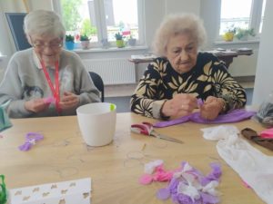 seniorki Dziennego Domu Pomocy naciągają kolorowe rajstopy na formę z drutu