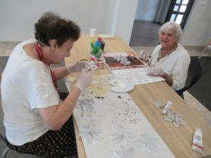 seniorki Dziennego Domu malują papierowe elementy pracy wykonywanej na zajęciach terapii zajęciowej
