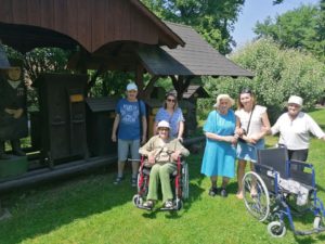 seniorzy Dziennego Domu stoja razem z opiekunami na tle zabytkowych uli
