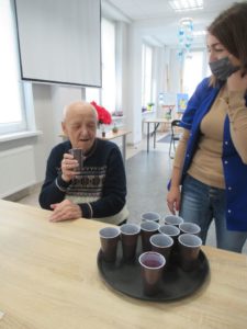 terapeuta zajęciowy częstuje seniora Dziennego Domu Pomocy sokiem z kiszonych buraczków czerwonych