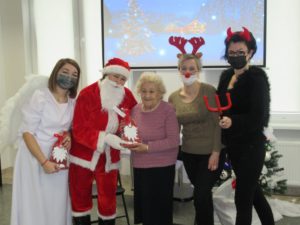 Mikołaj, wspólnie z pracownikami Dziennego Domu oraz seniorką prezentują prezent otrzymany z okazji Mikołajek