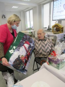 opiekun Dziennego Domu Pomocy przekazuje upominek seniorowi na Spotkaniu wigilijnym