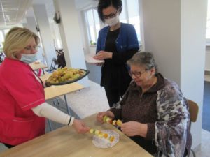 opiekunowie Dziennego Domu Pomocy częstują owocowymi szaszłykami seniorkę