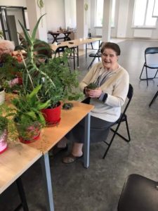 seniorka prezentuje kwiaty stojące na sali Dziennego Domu Pomocy dla Osób Starszych w Jaśle