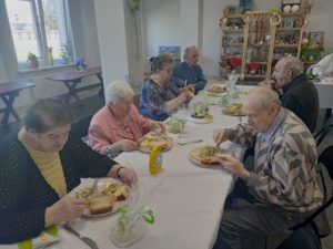 seniorzy Dziennego Domu Pomocy wspólnie świętują, jedząc potrawy w trakcie śniadania wielkanocnego
