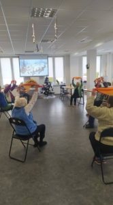 seniorzy dziennego Domu uczestniczą w ćwiczeniach ruchowych, z wykorzystaniem kolorowych chust