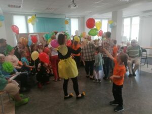 pracownik Dziennego Domu Pomocy rozdaje kolorowe balony dzieciom zaproszonym z okazji Dnia Dziecka