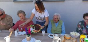 pracownik Dziennego Domu Pomocy w Jaśle częstuje seniorów upieczoną na grillu kiełbasą