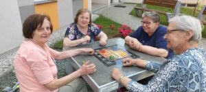 seniorki Dziennego Domu Pomocy w Jaśle siedzą przy stoliku, na którym przygotowana jest gra Chińczyk