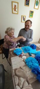 seniorzy Dziennego Domu Pomocy w Jaśle przygotowują kwiaty z niebieskiej bibuły na zajęciach terapii zajęciowej