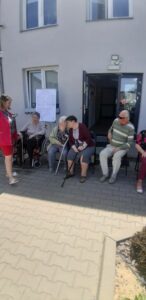 seniorzy Dziennego Domu Pomocy wspólnie z opiekunką biorą udział w zabawie Głuchy telefon
