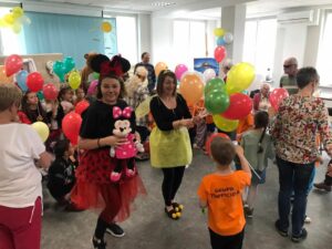 seniorzy Dziennego Domu Pomocy wspólnie z pracownikami rozdają kolorowe balony dzieciom zaproszonym z okazji Dnia Dziecka